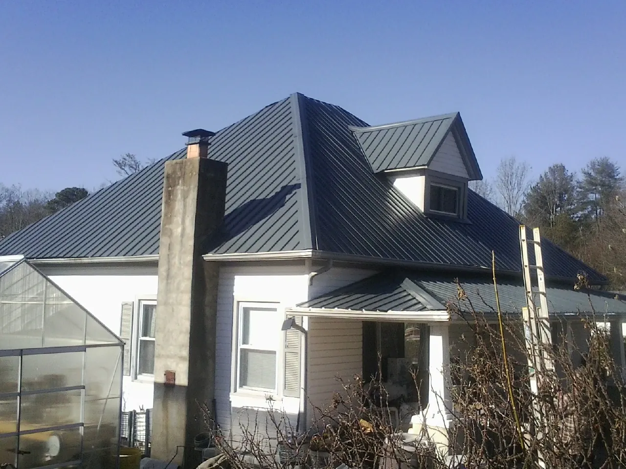 Dark blue standing seam metal roof on a white farmhouse with dormer — Slate & Tile Roof Repair by Roofing Brothers in Pinebluff
