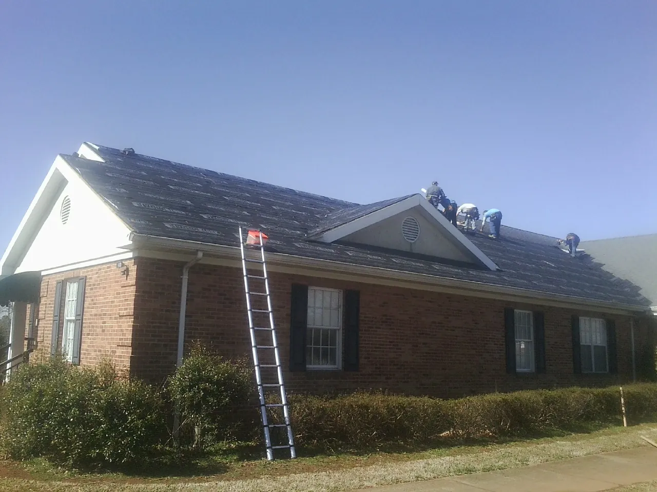 Crew tearing shingles off a brick ranch roof with a ladder set — Emergency Roof Repair work by our crew in Pinebluff