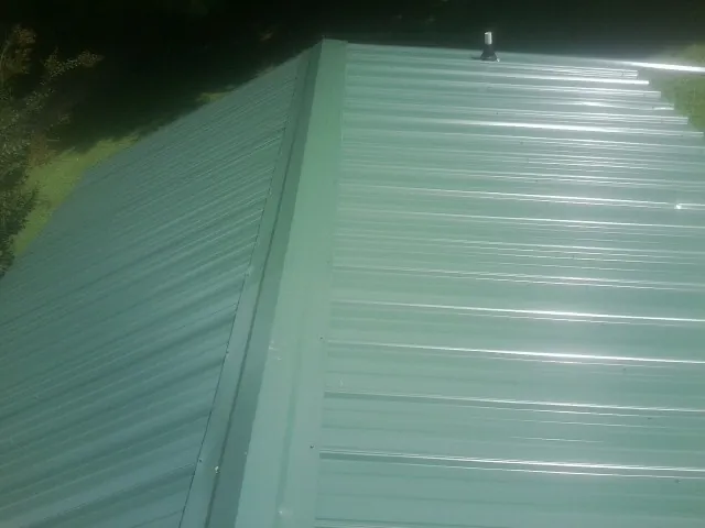 New green metal panels meeting at the ridge of a roof — Flat Roof Repair work by our crew in Pinebluff